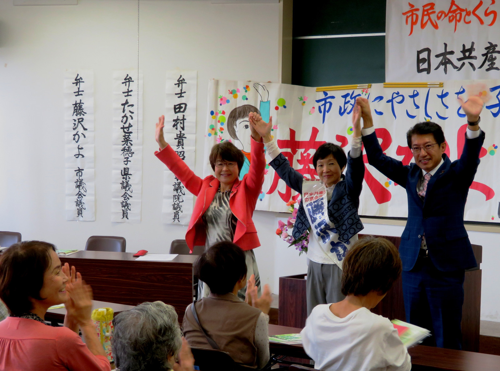 参加者の拍手に手を上げて応える（右から）田村、藤沢、高瀬の各氏＝１５日、北九州市