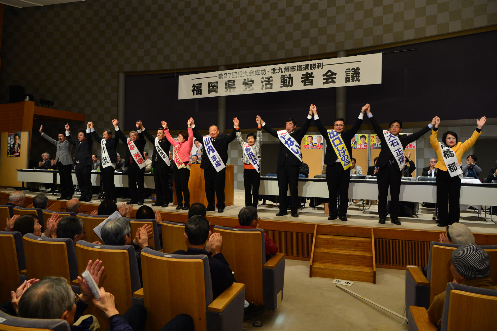 満場の拍手に応える（左から）田村、仁比両氏と10人の市議候補＝7日、北九州市