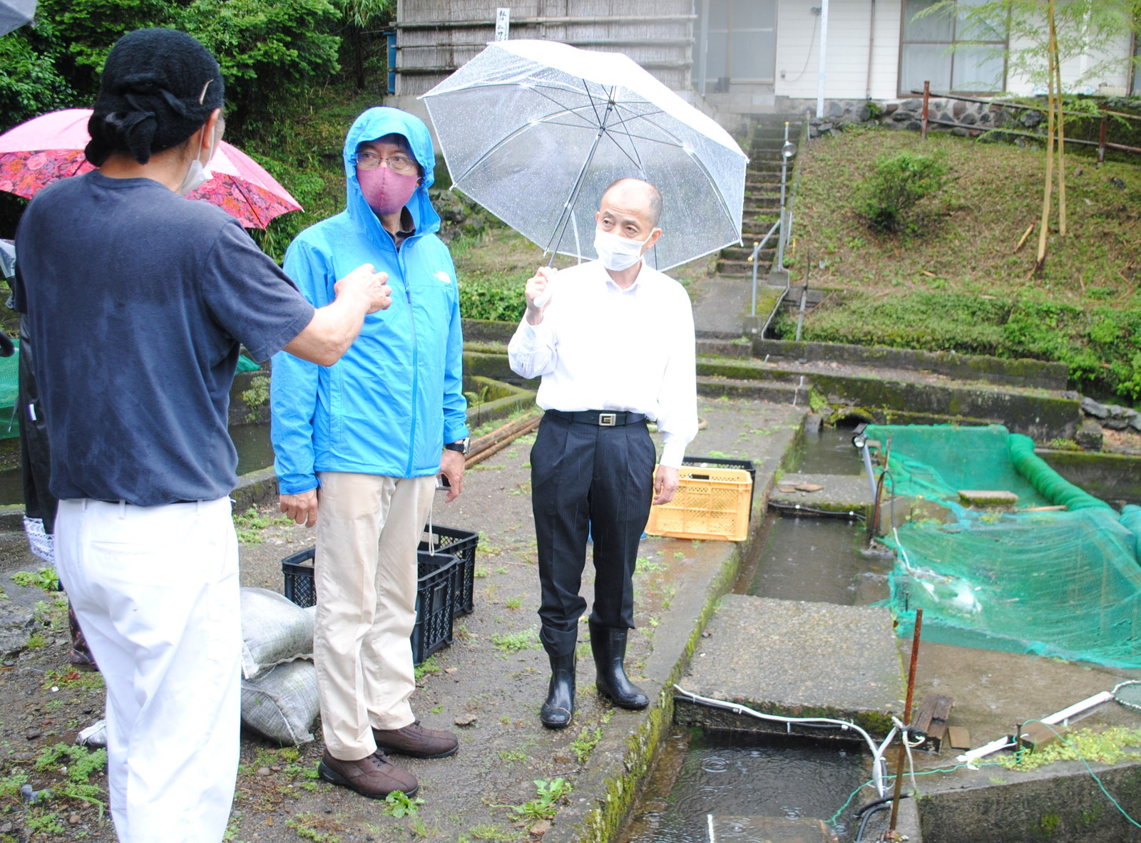 養魚業者（左端）から話を聞＜（右へ）田村衆院議員、松本候補＝12日、都城市