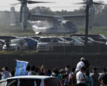 木更津駐屯地に着陸した陸上自衛隊のV22オスプレイ。手前は｢オスプレイはいらない｣と抗議する人たち＝2020年７月10日、千葉県木更津市