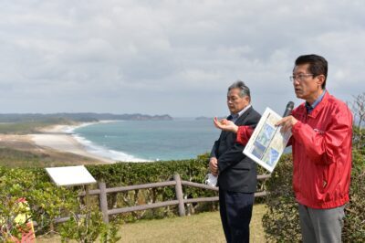 訓練が予定されている海浜公園（奥）を背に訓練中止を訴える（右から）田村、山内両氏＝１日、鹿児島県南種子町